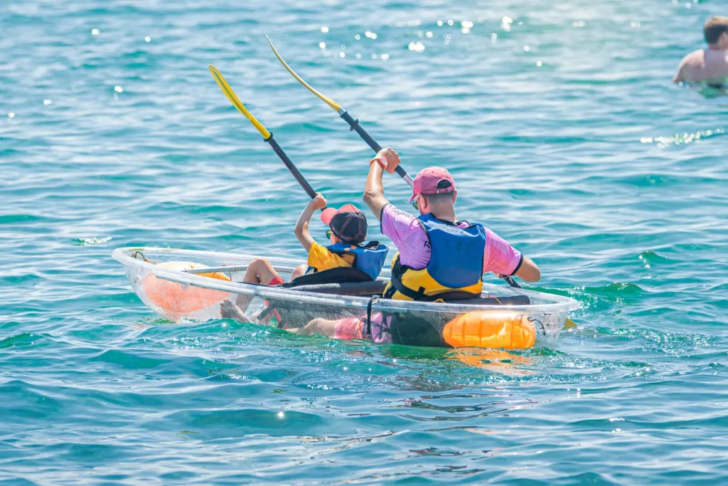 Kayak transparent en Corse - activité familliale Un adulte et un enfant dans un kayak transparent pagayant sur une eau bleue en Corse.