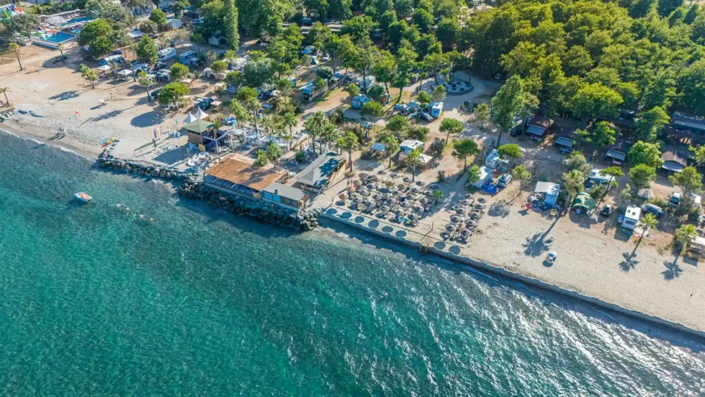 camping-merendella-vue-du-ciel-eau-turquoise-et-azur-avec-plage-de-sable-fin Vue aérienne d'un camping de luxe en Corse en bord de mer avec hébergements sous les arbres, plage de sable fin aménagée et eau turquoise.