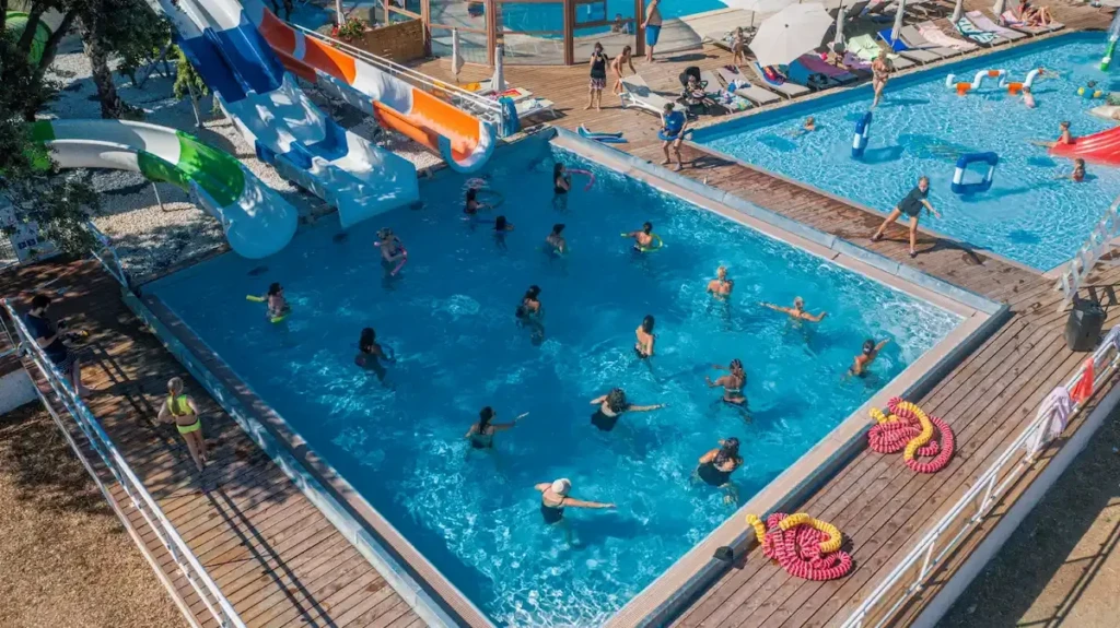 parc-aquatique-aquagym-merendella Séance d'aquagym animée dans la piscine d'un camping en Corse avec toboggans aquatiques en arrière-plan.
