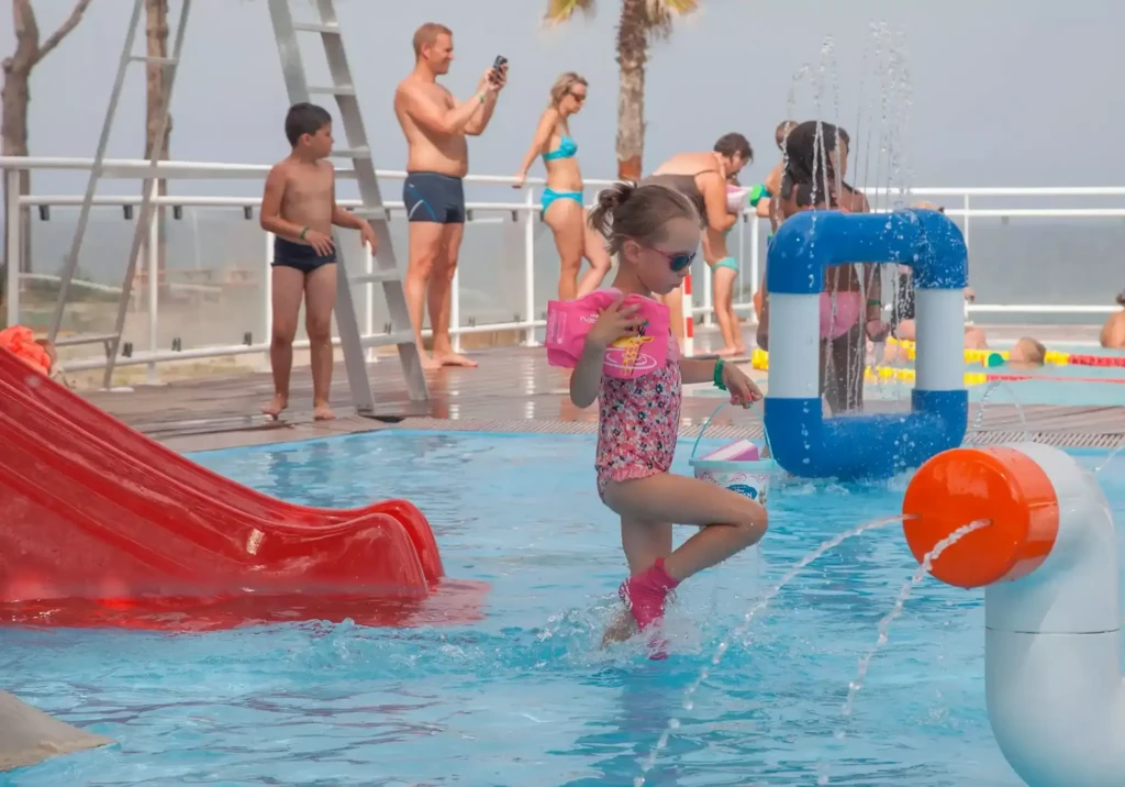 parc-aquatique-pataugeoire-enfants Petite fille avec brassards roses marchant dans la pataugeoire et les jeux d'eau d'un camping corse.