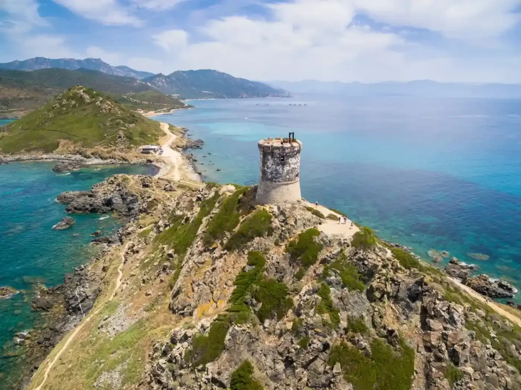 tour-genoise-littoral-corse-randonnee Vue aérienne d'une tour génoise historique surplombant une mer turquoise et un littoral sauvage en Corse.