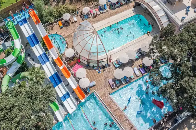 piscine-chauffee-couverte-merendella Vue plongeante sur le parc aquatique d'un camping en Corse comprenant plusieurs bassins, des toboggans géants et une piscine couverte chauffée.