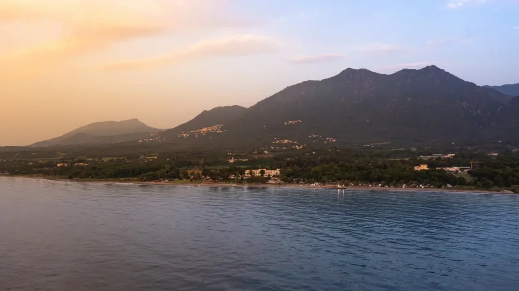 Vue aérienne du littoral des plus belles plages autour de San-Nicolao en Corse, avec la mer calme et les montagnes en arrière-plan au coucher du soleil.