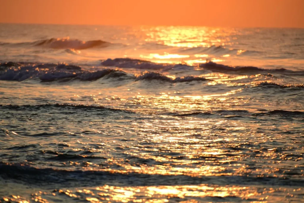 Reflets dorés du soleil couchant sur les vagues de la plage de Poggiole en Corse.