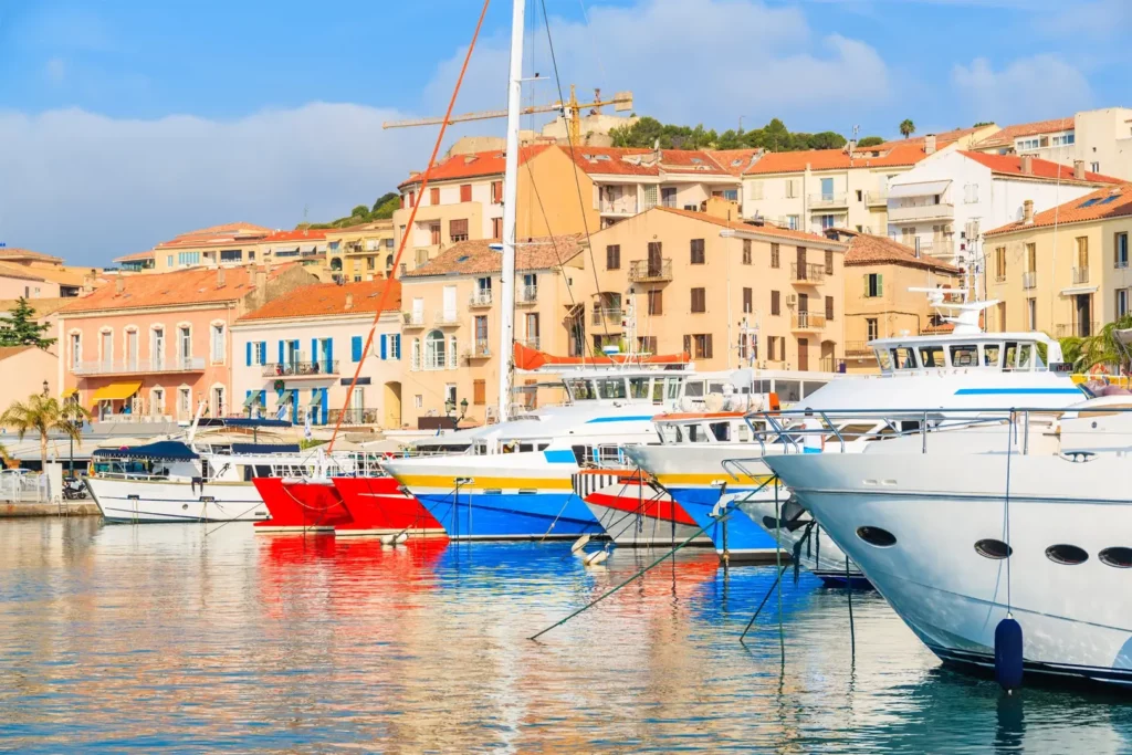 Voiliers colorés amarrés dans le port de Calvi, en Corse, devant les maisons aux façades méditerranéennes. Départ de la plus longue traversée
