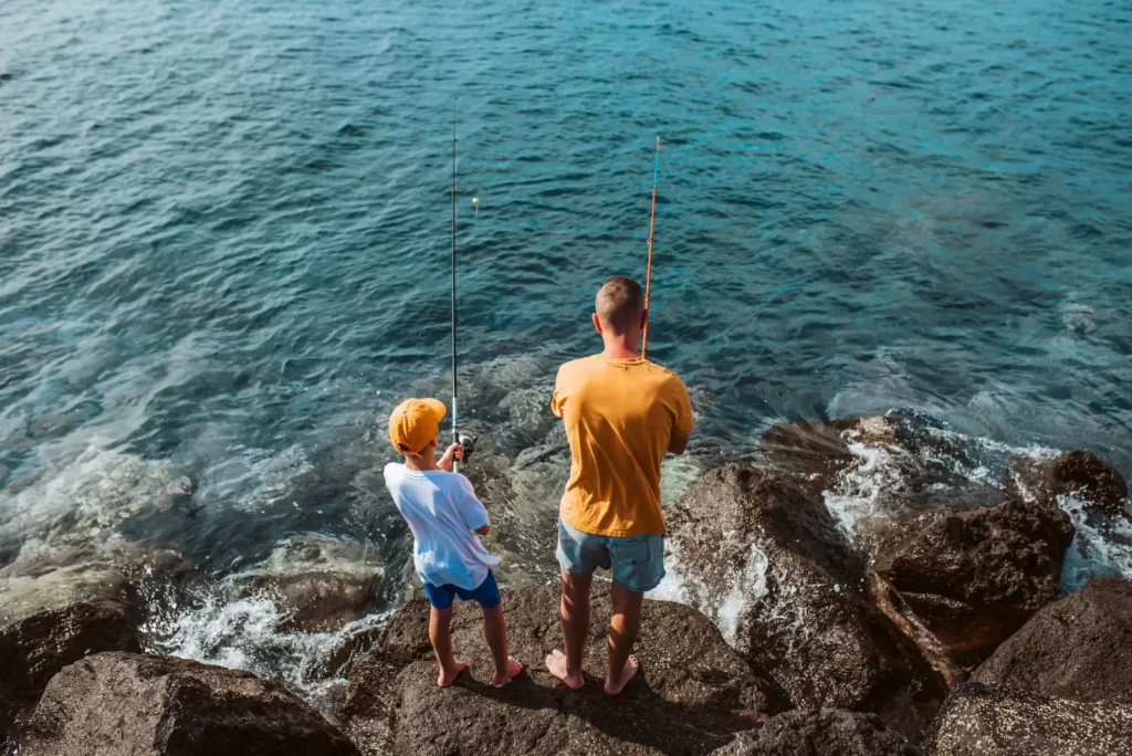 Peche familialle en Corse Un adulte et un enfant pêchent ensemble sur des rochers au bord de la mer en Corse.